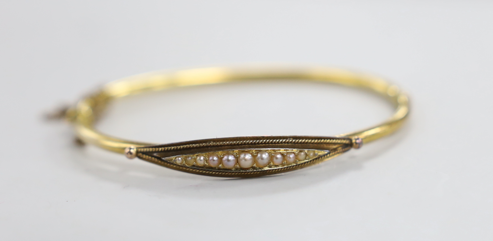 An Edwardian 15ct and graduated seed pearl set hinged bangle